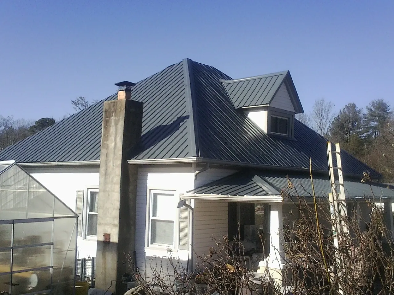 Dark blue standing seam metal roof on a white farmhouse with dormer — Slate & Tile Roof Repair by Roofing Brothers in State Road