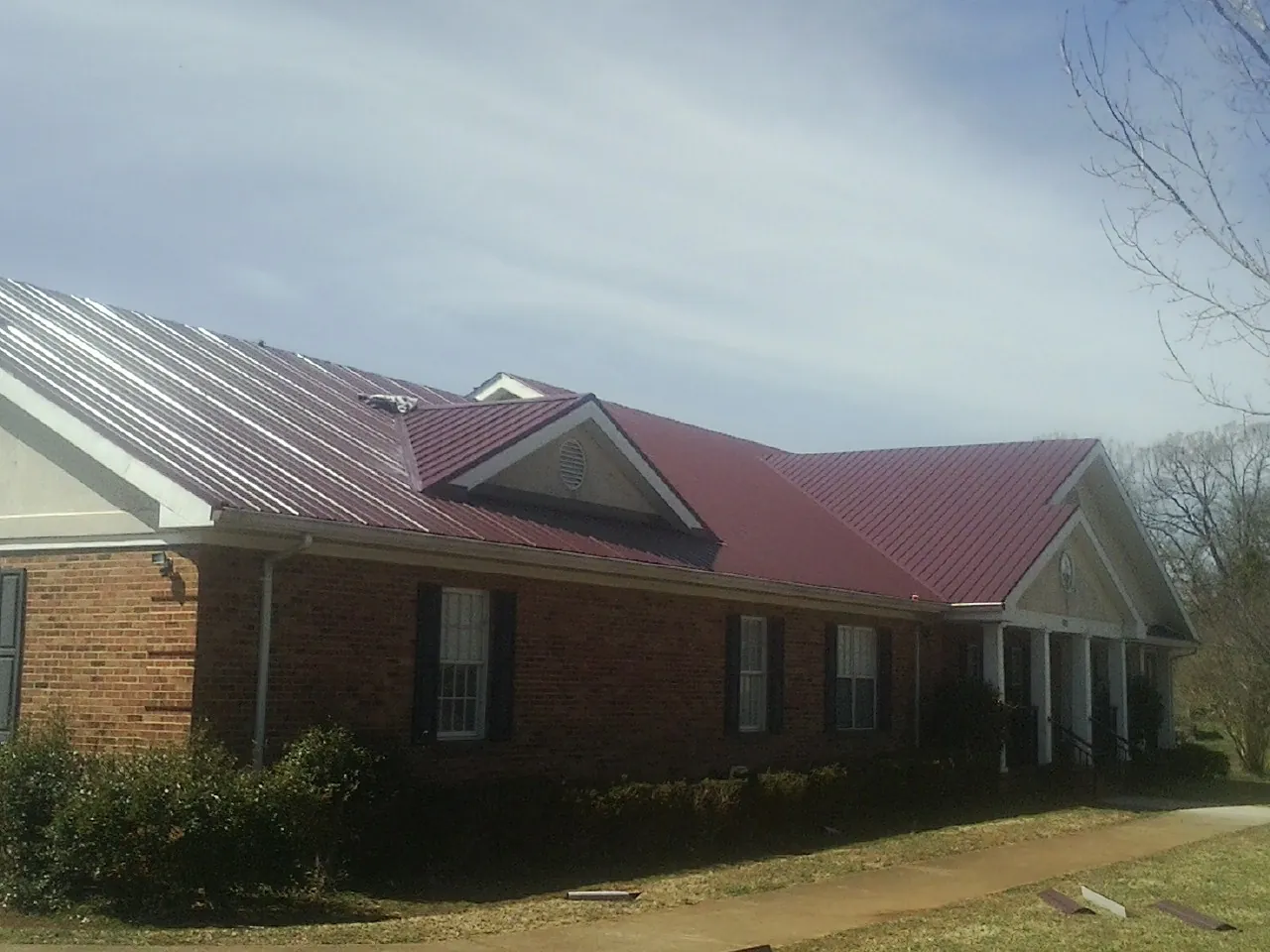 Red metal roof with gabled entries on a long brick building, from a Hail Damage Roof Repair job in State Road