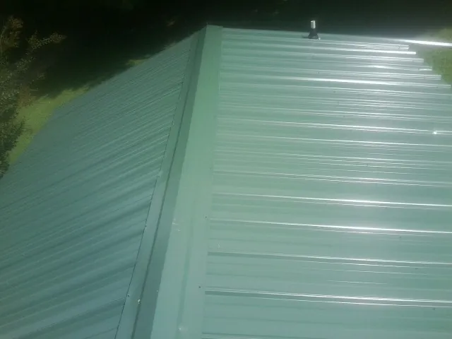 New green metal panels meeting at the ridge of a roof — Flat Roof Repair work by our crew in State Road